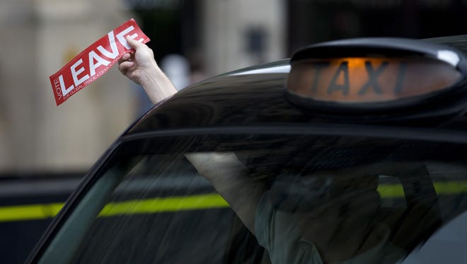 A taxi driver holds a sticker for the "Vote Leave" pro-Brexit campaign as he drives past news media in London on June 22, 2016.