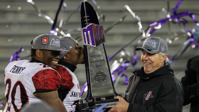 San Diego State's  Rashaad Penny (20), Damontae Kazee (23) and head coach Rocky Long lift the championship trophy after defeating Wyoming.