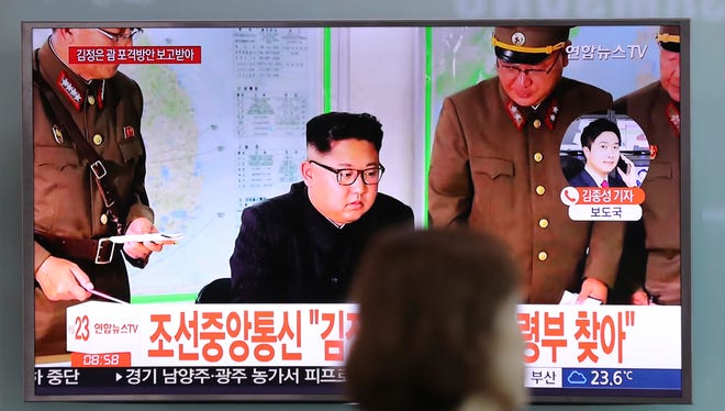 A woman walks by a TV screen showing a local news program reporting about North Korean military's plans to launch missiles into waters near Guam, with an image of North Korean leader Kim Jong Un, at Seoul Train Station in Seoul, South Korea, Tuesday, Aug. 15, 2017.