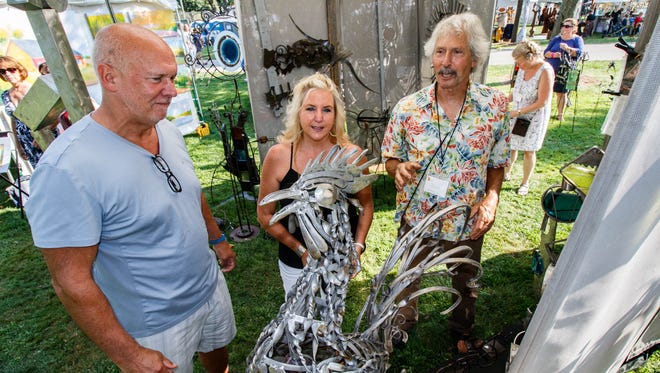 Sculptor Don Esser (right) of Waunakee talks with longtime customers Frank Hojnacki and Veronique Swofford of Oconomowoc about their latest purchase during the 47th annual Oconomowoc Festival of the Arts in Fowler Park on Saturday, August 19, 2017.