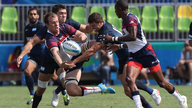 Ben Pinkelman of the United States, left, passes the ball to teammate Perry as he is being tackled during a rugby sevens match against Argentina at Deodoro Stadium in the Rio 2016 Summer Olympic Games.