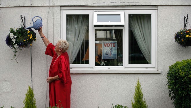 Barbara House who supports Brexit, waters her plants outside her house while a poster advertising Britain leaving the EU is attached to her window in Headington outside Oxford on June 23, 2016. Millions of Britons began voting today in a bitterly-fought, knife-edge referendum that could tear up the island nation's EU membership and spark the greatest emergency of the bloc's 60-year history.