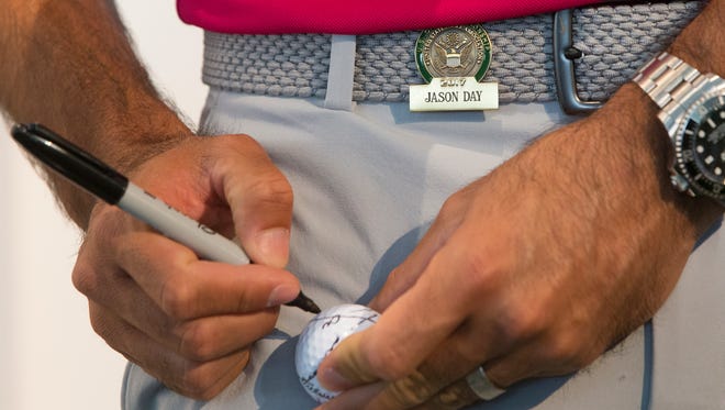 Jason Day signs a golf ball during a promotional appearance for Lexus during practice rounds.