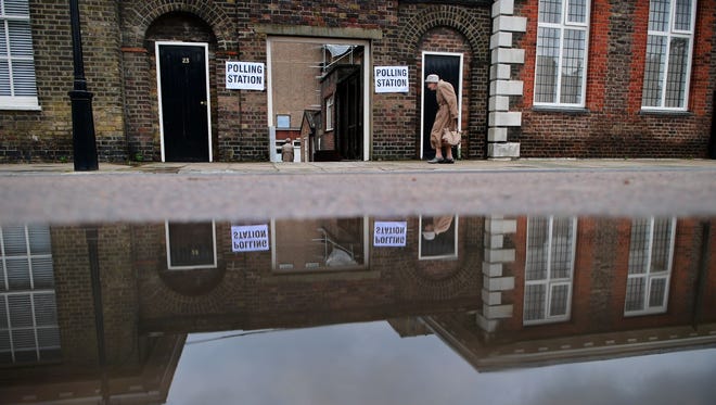 An elderly woman is reflected in a puddle of rain water as she arrives at a polling station at the Royal Hospital in Chelsea, west London, as Britain holds a referendum to vote on whether to remain in or to leave the European Union.