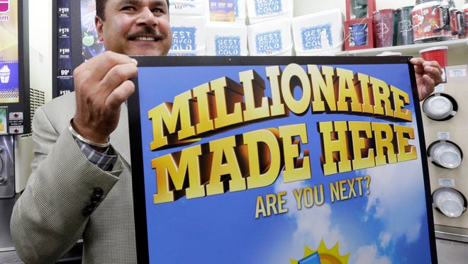 Balbir Atwal, the owner of a 7-Eleven store that sold a winning Powerball lottery ticket, holds up a Millionaire Made Here, sign at his store in Chino Hills, Calif.